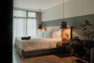 A neatly made bed with pillows and a blanket, a bedside table with a lamp, and a wall-mounted phone.