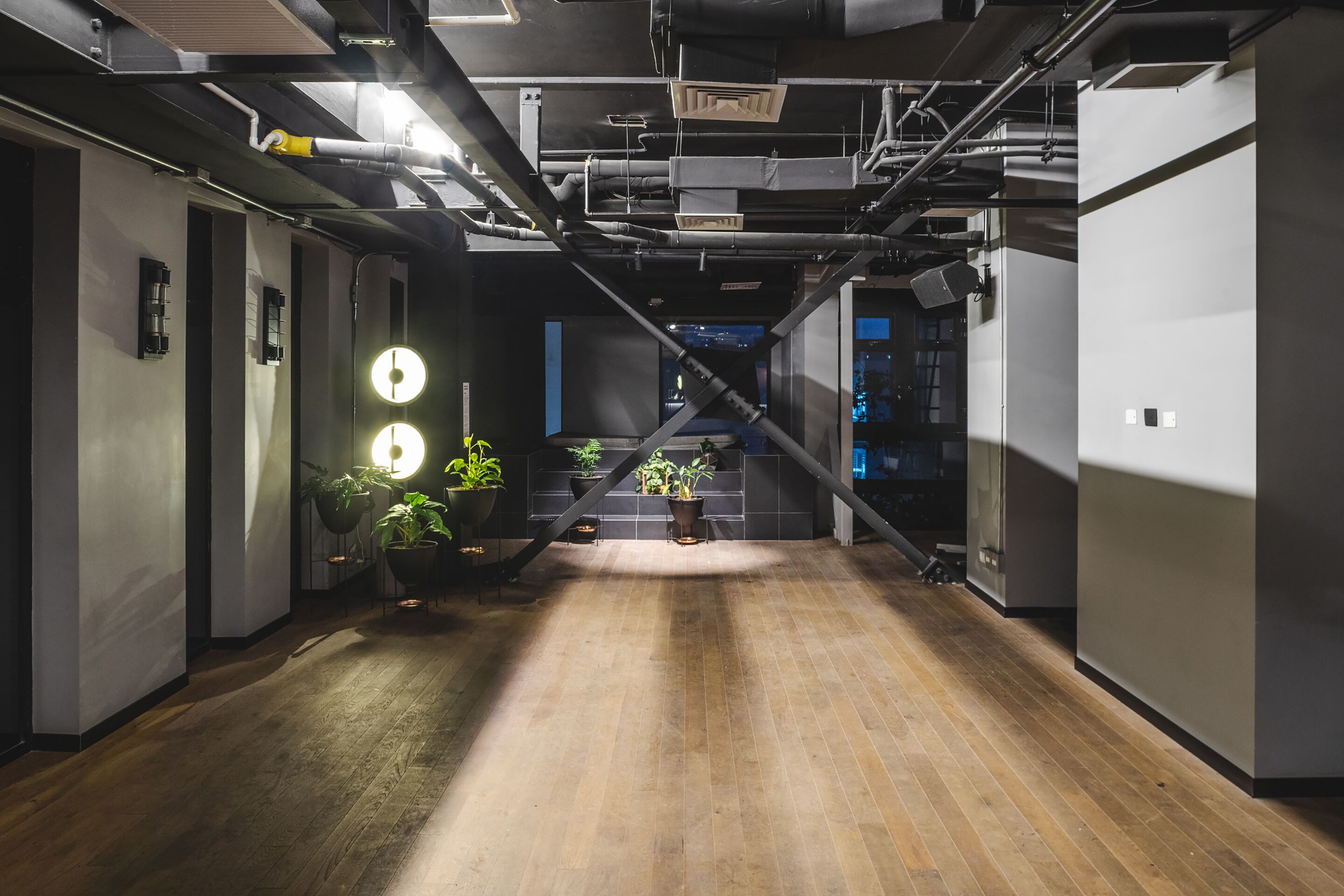 A modern interior with exposed ductwork, wooden flooring, and potted plants.