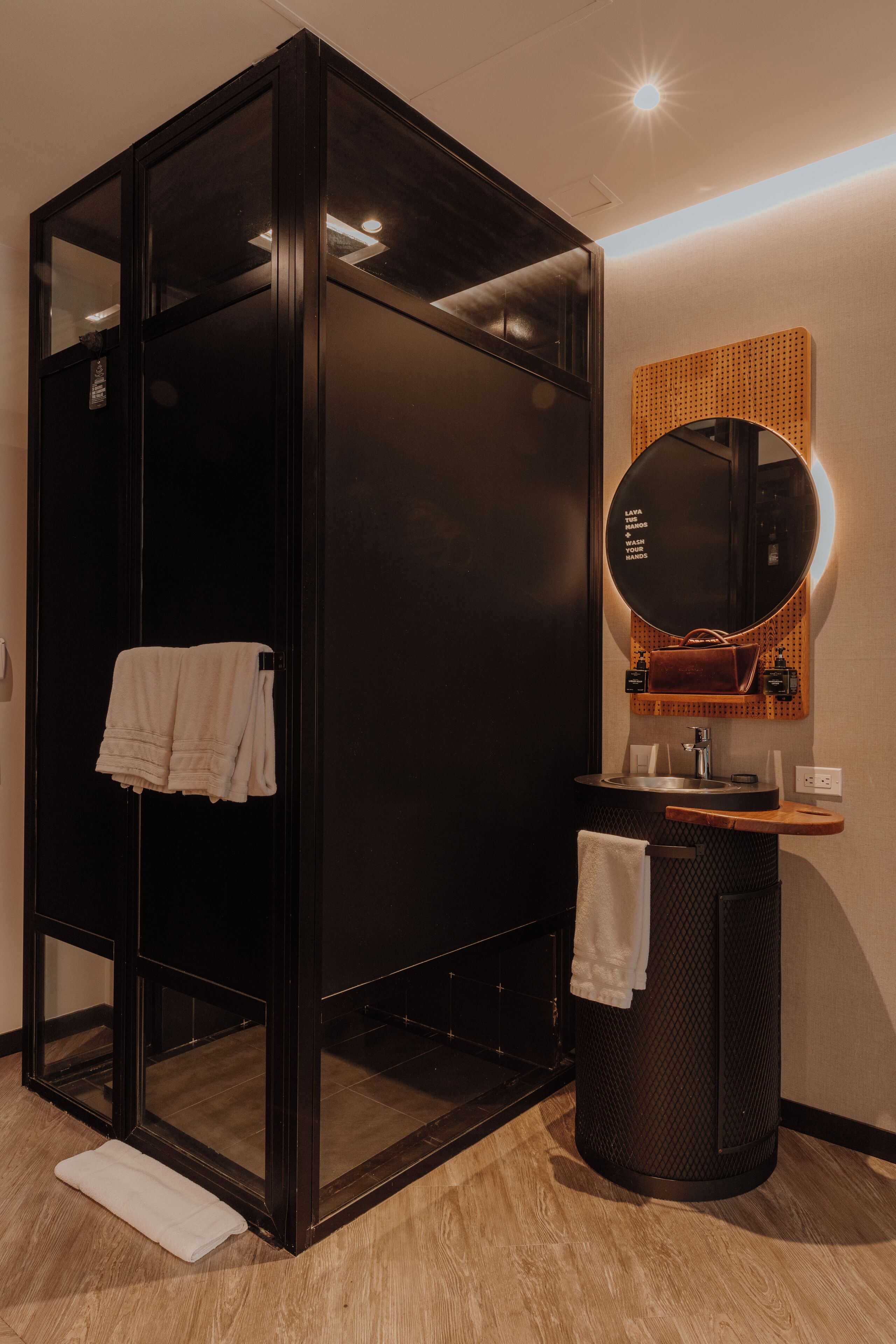 Een moderne badkamer met een douchecabine van glas, een ronde spiegel en een houten wastafelmeubel.