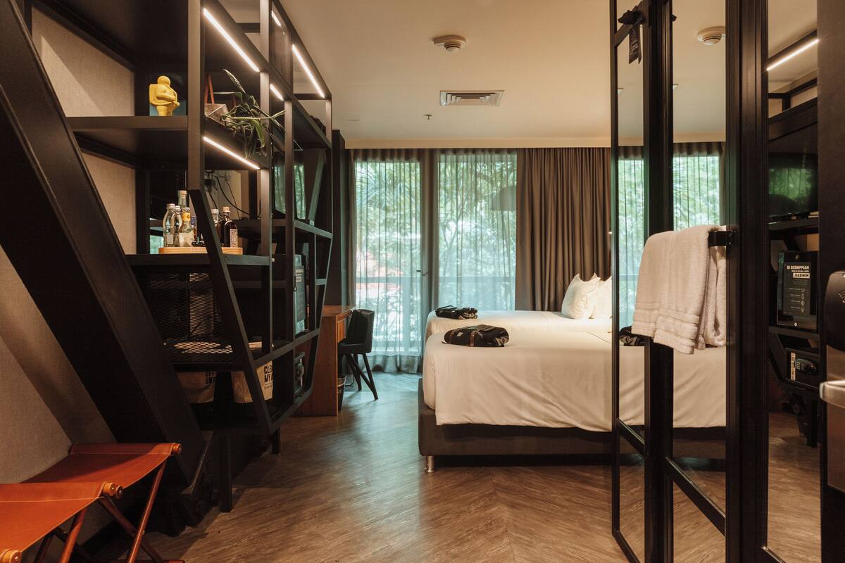 A modern hotel room with a large bed, a desk, and a bookshelf.