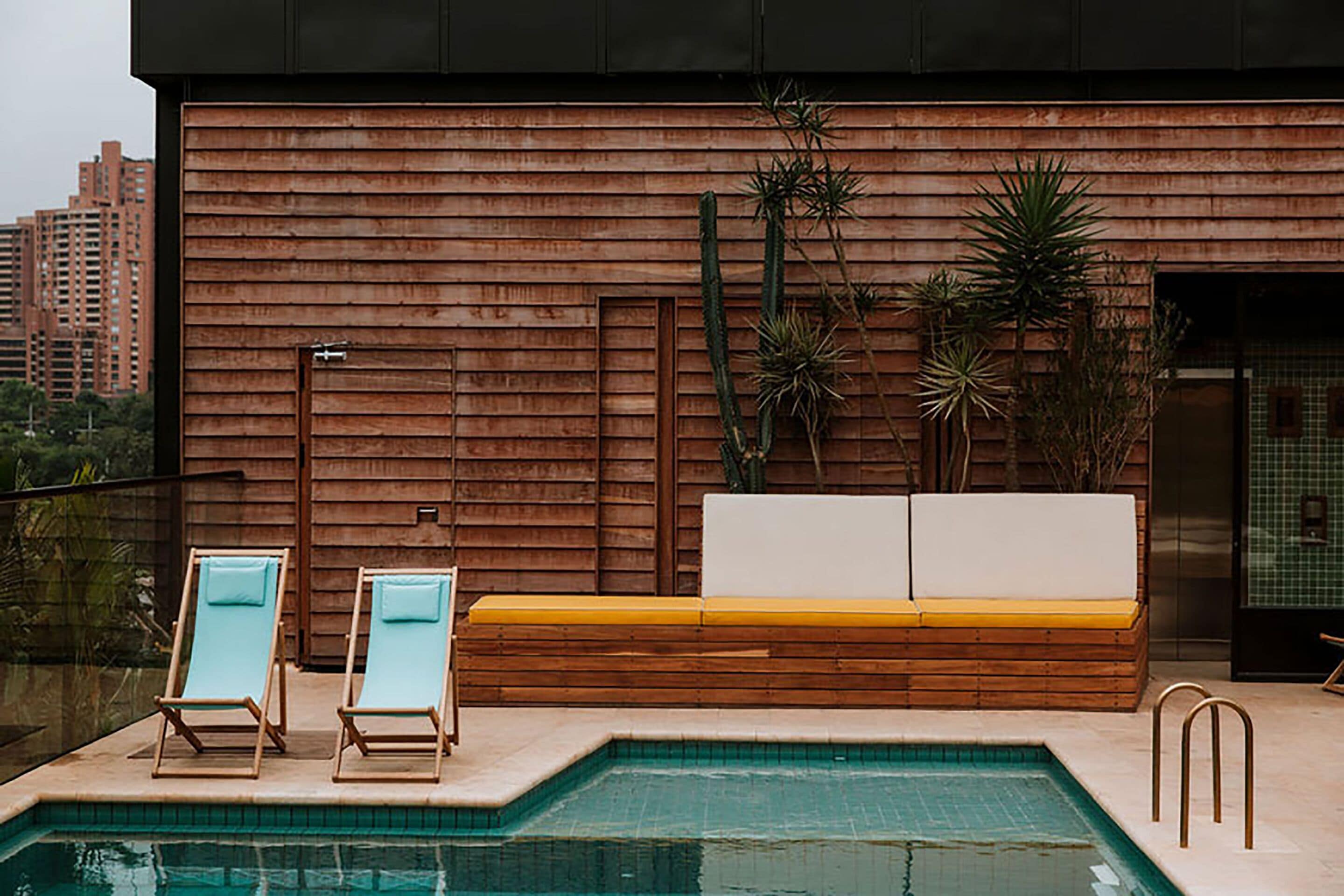 A pool area with two lounge chairs and a wooden bench with cushions.