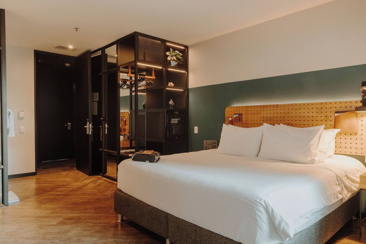 A hotel room with a large bed, a wooden headboard, a built-in wardrobe, and a small desk with a lamp.