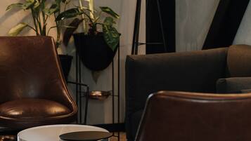 A modern living room with a brown leather armchair, a small round table, a floor lamp, and potted plants.