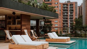 Un área junto a la piscina con tumbonas de madera y una zona de estar integrada con una mesa y sillas.