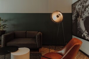 Una sala de estar moderna con una pared de acento verde oscuro, un sofá de cuero marrón, una mesa de centro redonda, una lámpara de pie y una fotografía en blanco y negro enmarcada.