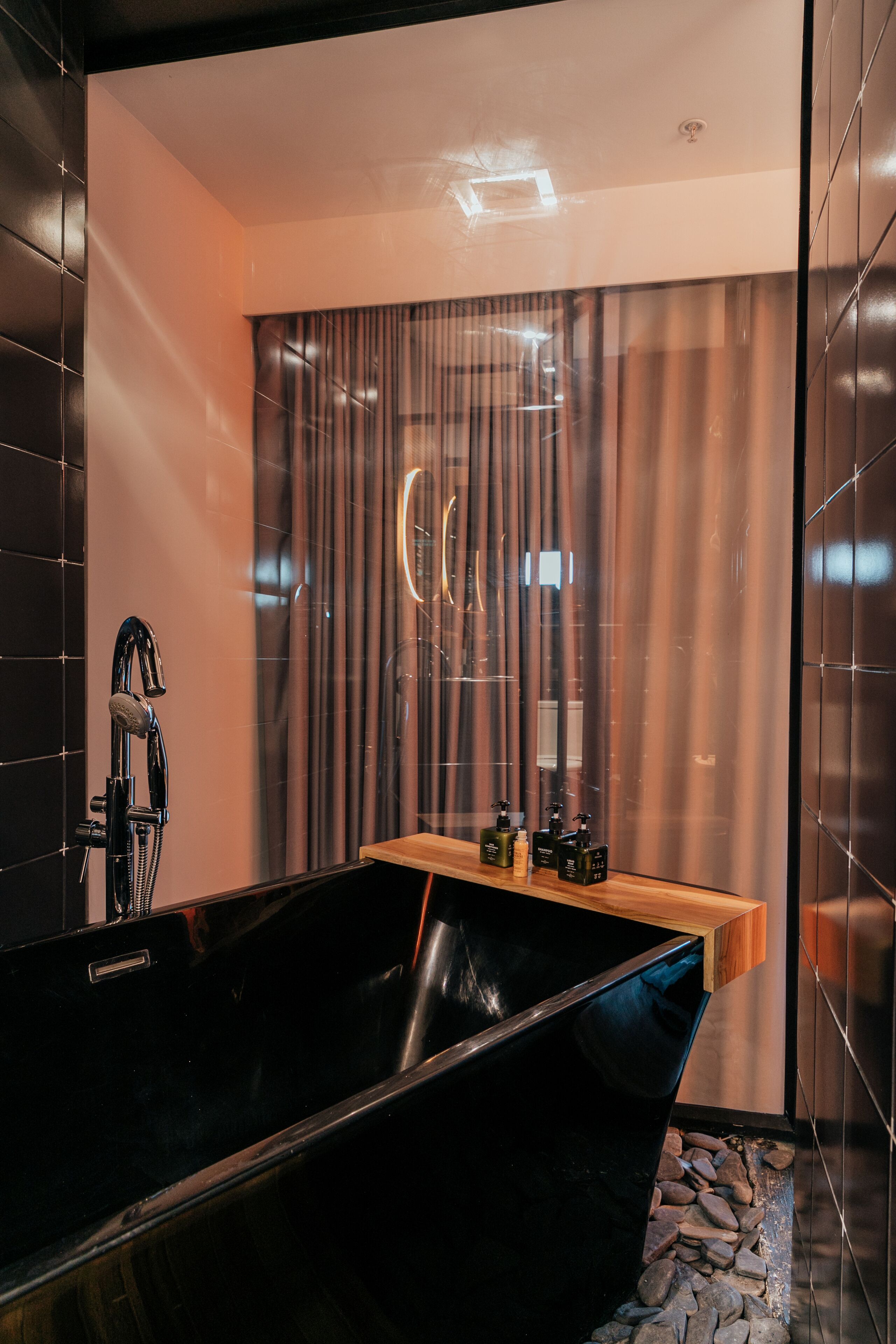 A modern bathroom with a black bathtub, a wooden vanity, and a mirror with a circular design.