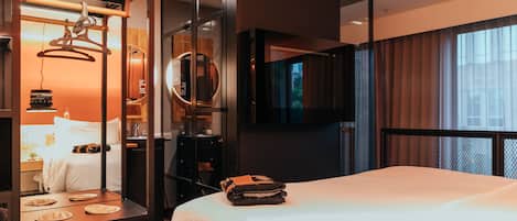 A modern hotel room with a large bed, a TV mounted on the wall, and a mirror above the bed.