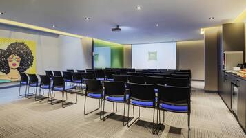 A conference room with rows of chairs, a projector screen, and a presentation screen.