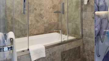 Un baño moderno con ducha envuelta en vidrio, bañera y tocador de vidrio con una toalla.
