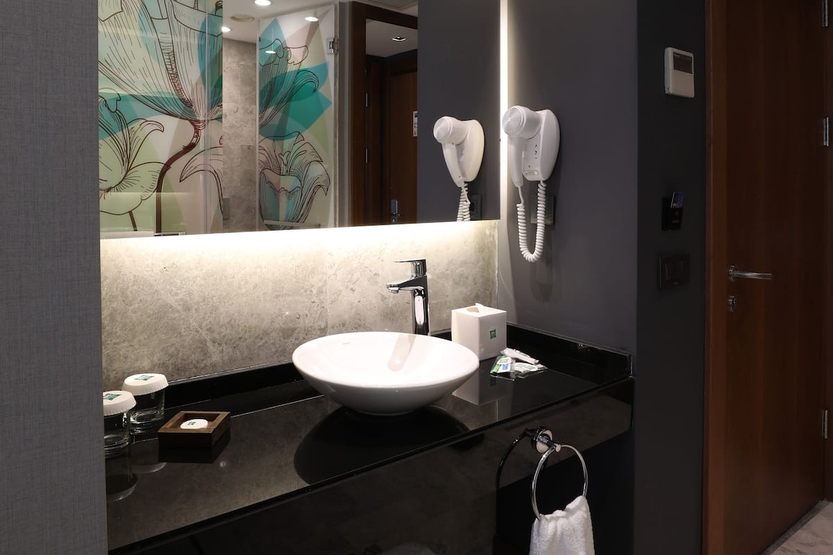 Un baño moderno con un espejo grande, un lavabo blanco y un secador de pelo montado en la pared.