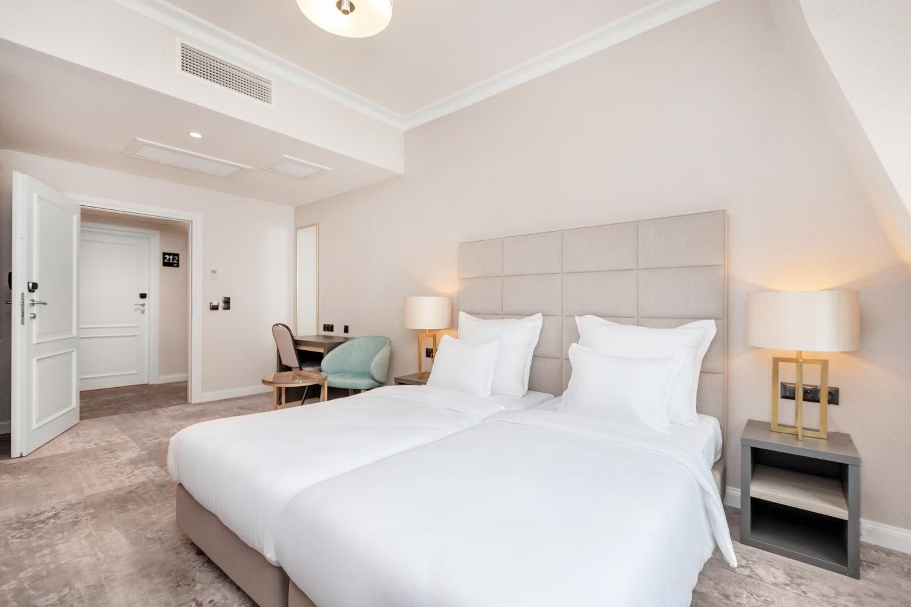 Una camera d'albergo con un letto grande, due comodini con lampade, una sedia e una scrivania.