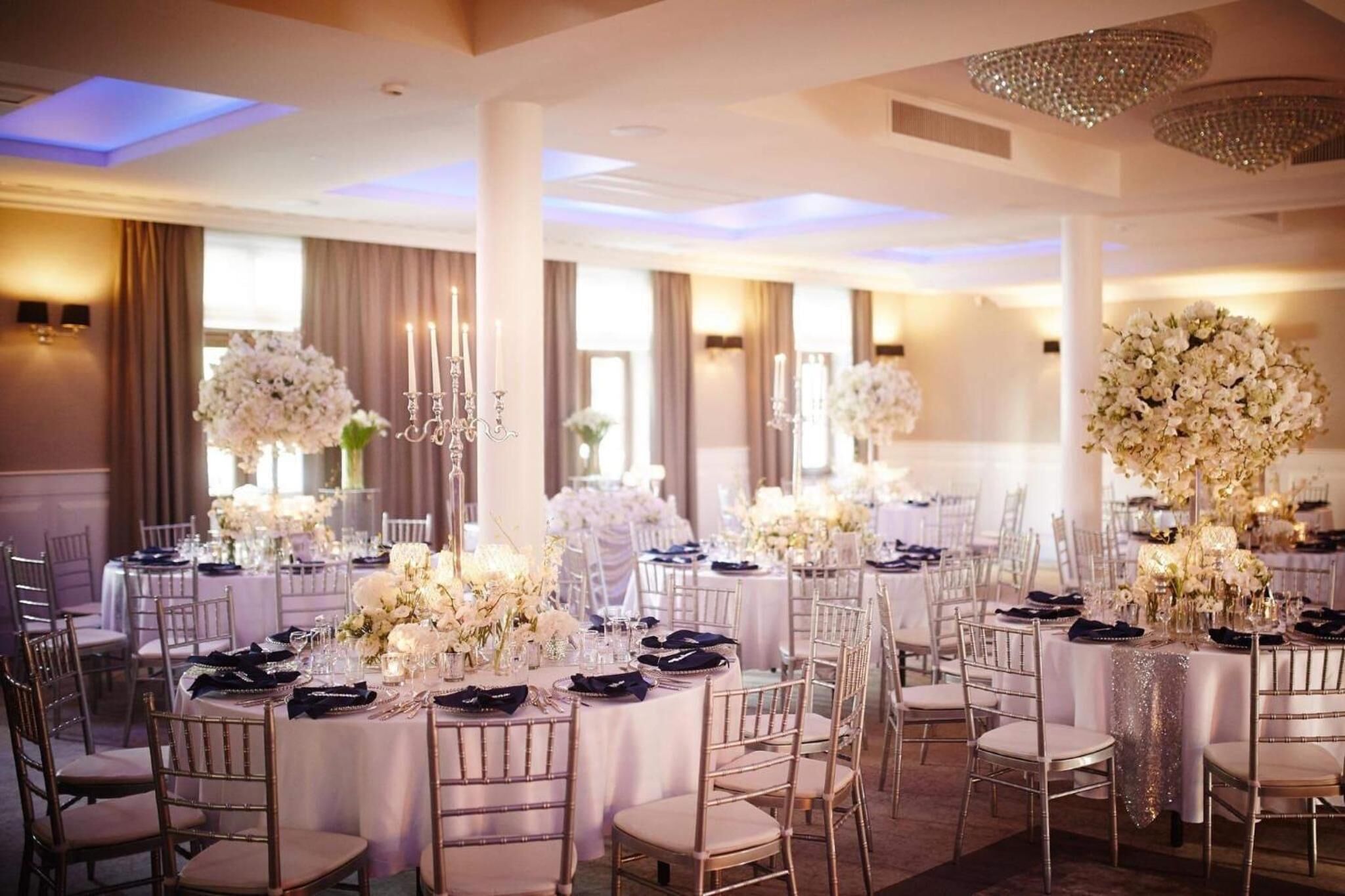 Une salle de banquet avec des tables rondes, des nappes blanches et des centres de table floraux.
