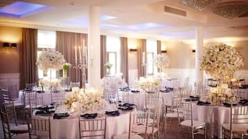 Une salle de banquet avec des tables rondes, des nappes blanches et des centres de table floraux.