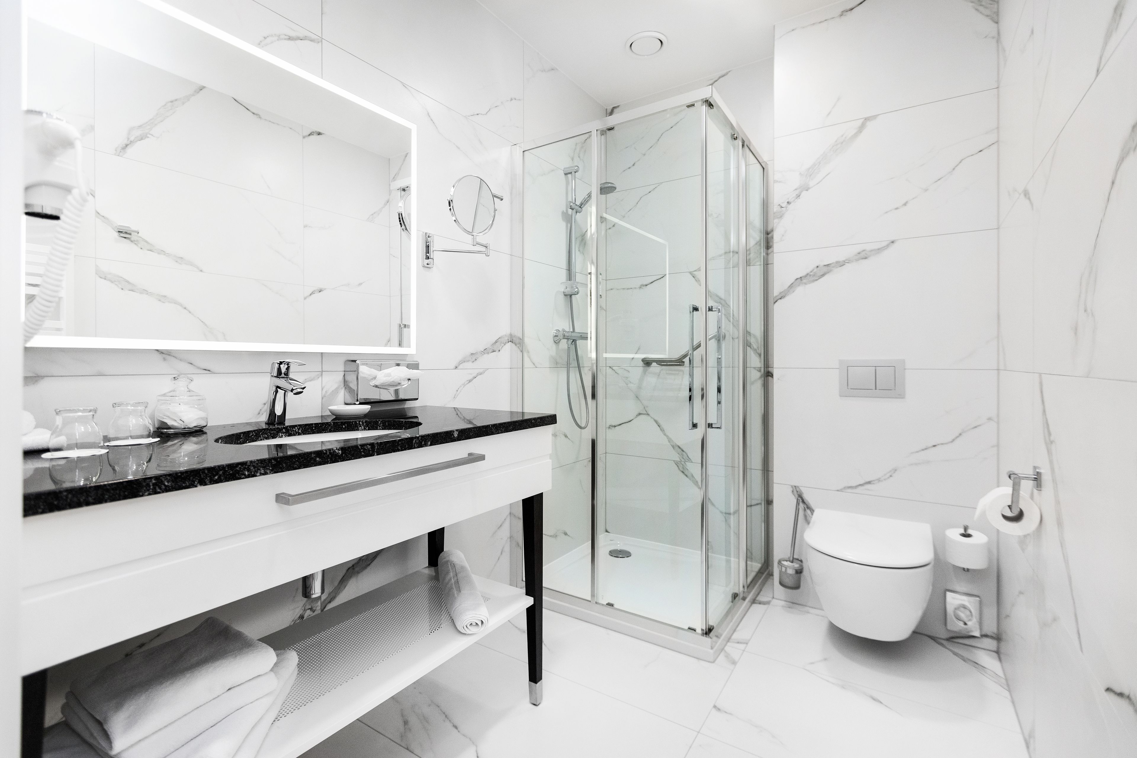 A modern bathroom with a glass shower enclosure, a white sink with a black countertop, and a large mirror.