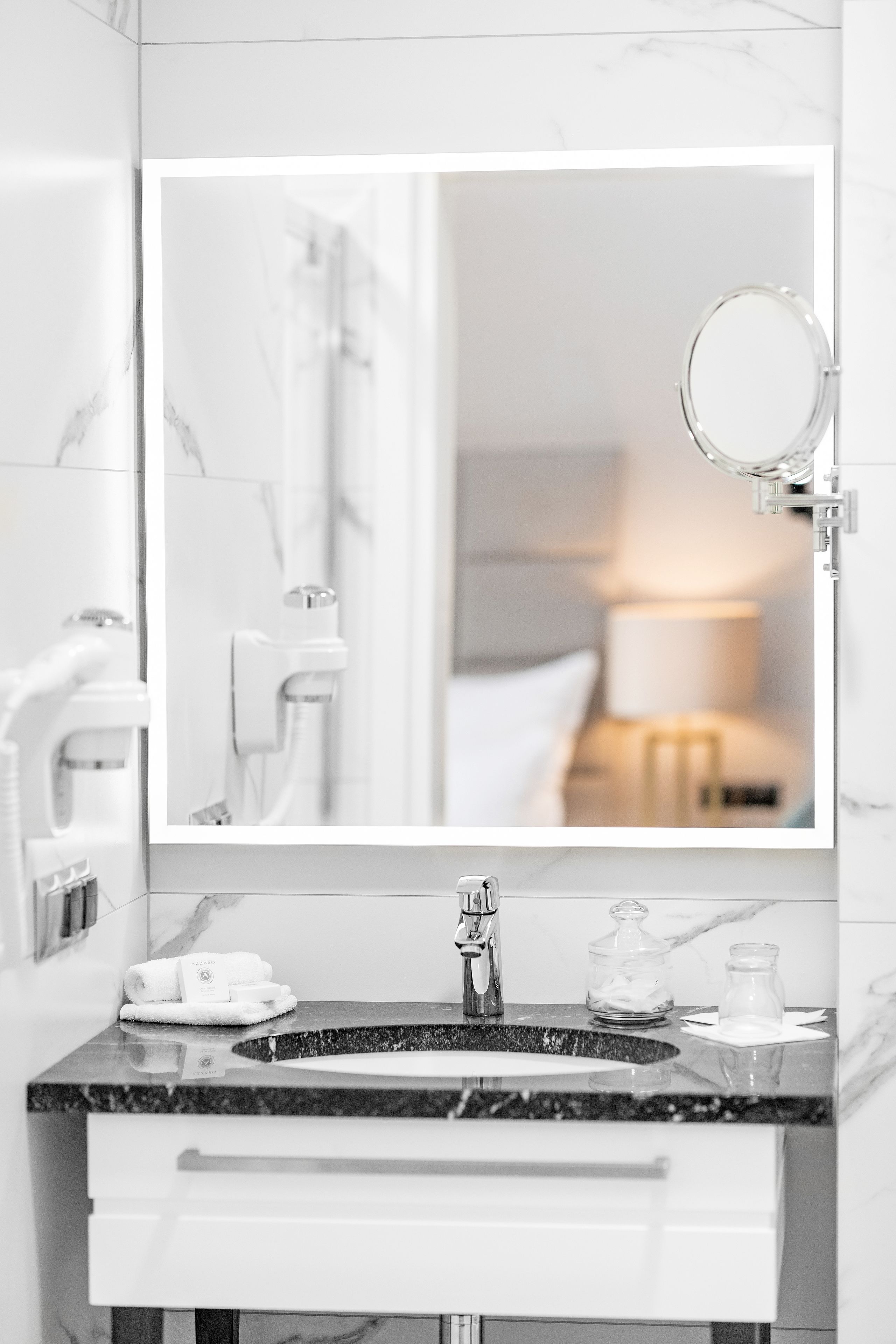 A modern bathroom with a marble sink, a large mirror, and a towel rack.