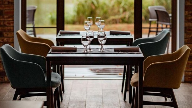 Comedor con un amplio ventanal, una mesa servida con copas de vino y sillas.