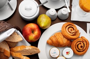 Morgenmad med croissanter, et æble, en pære og et glas marmelade.