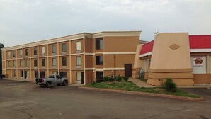 Ein mehrstöckiges Hotel mit Parkplatz, ein daran angrenzendes Gebäude mit rotem Dach und ein silberner Pickup-Truck auf dem Parkplatz.