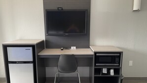 Ein kleines Zimmer mit Schreibtisch, Stuhl, Kühlschrank und Mikrowelle.