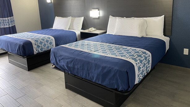 Ein Hotelzimmer mit zwei Betten, jeweils mit einer blau-weißen Bettdecke, weißen Kissen und einem Holz-Kopfende. Zwischen den Betten befindet sich ein Nachttisch mit Telefon und Lampe.