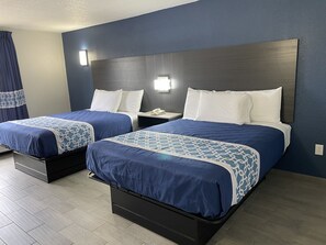A hotel room with two beds, each with a blue and white patterned bedspread, white pillows, and a wooden headboard. There is a nightstand with a phone and a lamp between the beds. - Executive Inn (Mount Pleasant)