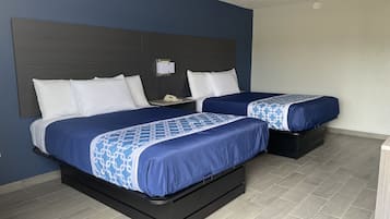 A hotel room with two beds, a dark headboard, a bedside table with a lamp, and a tiled floor.