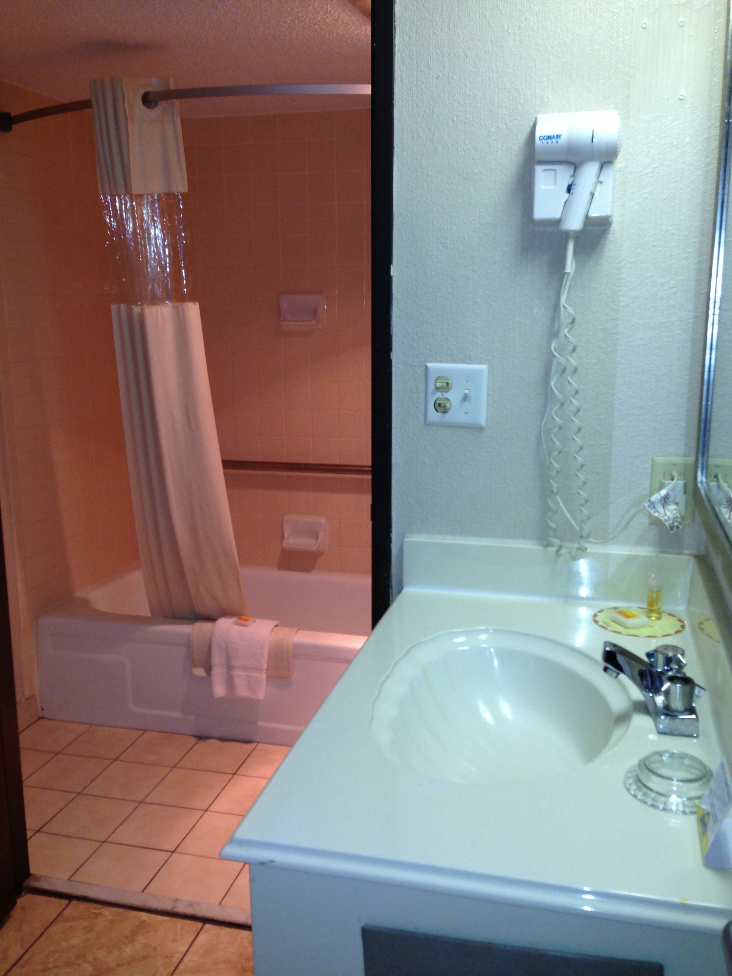 Une salle de bain avec une baignoire, un rideau de douche, un lavabo, un miroir et un sèche-cheveux fixé au mur.