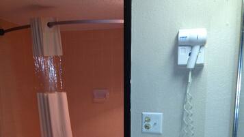 Une salle de bain avec une baignoire, un rideau de douche, un lavabo, un miroir et un sèche-cheveux fixé au mur.