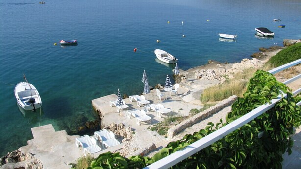 A coastal area with boats, a small beach with lounge chairs, and a rocky shoreline. - Apartments Villa Marija (Seget)