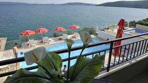 A pool area with red umbrellas, a view of the sea, and a person standing by the pool. - Apartments Villa Marija (Seget)