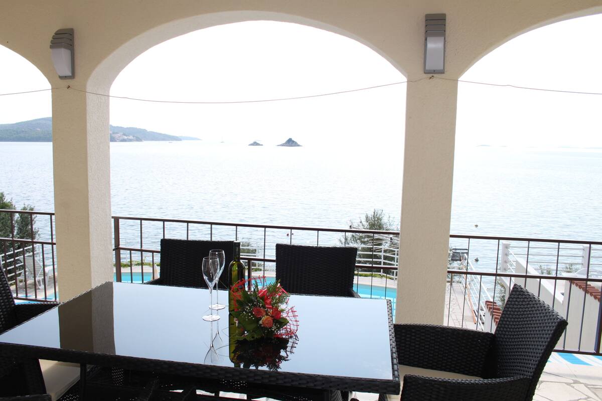 A balcony with a table and chairs, overlooking a body of water and distant islands.