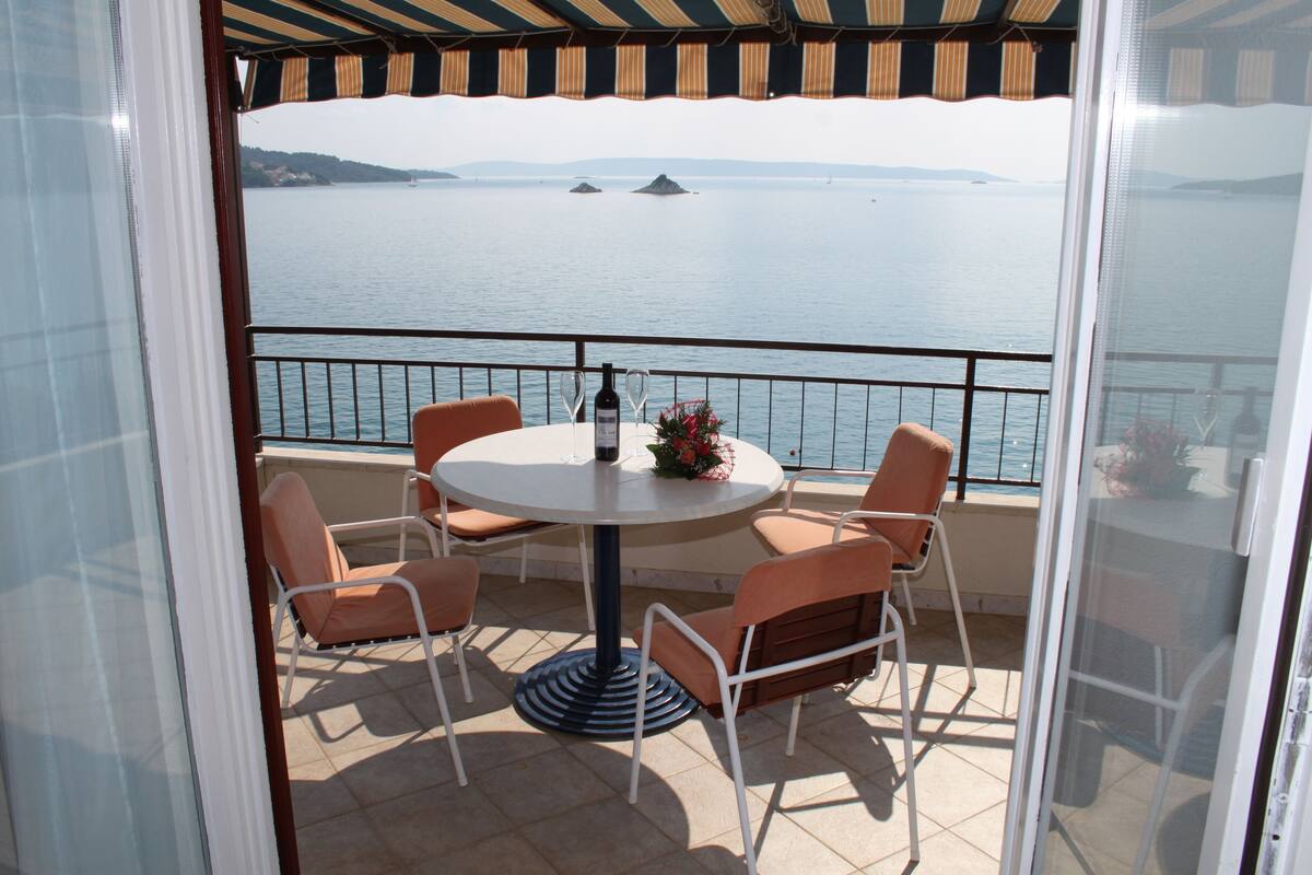 A balcony with a round table and chairs, overlooking a body of water with distant landforms.