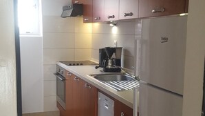 A kitchen with wooden cabinets, a built-in oven, a coffee maker, and a refrigerator. - Apartments Villa Marija (Seget)
