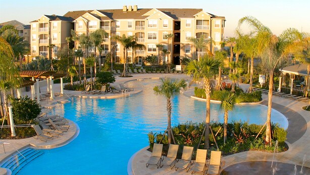 A resort with a central swimming pool, lounge chairs, and palm trees. - Sunderland Condo at Windsor Hills Resort (Kissimmee)