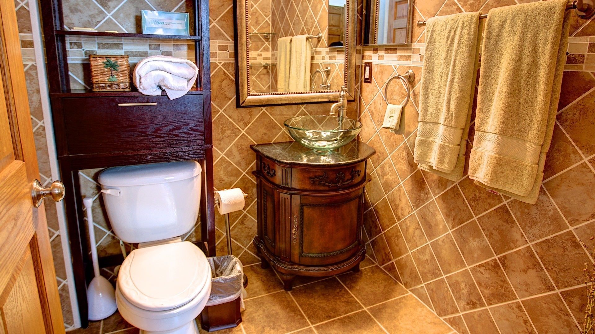A bathroom with a toilet, a wooden vanity with a glass bowl sink, and a tiled backsplash.