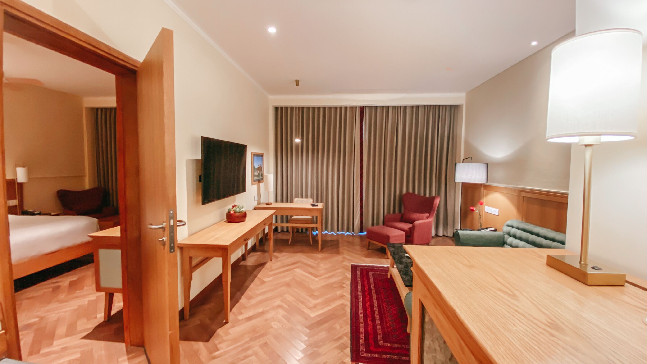 A hotel room with a bed, a desk, a chair, a sofa, a TV, and a window with curtains.