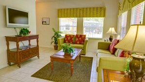A living room with a television, a wooden coffee table, a sofa, and a lamp. - Durham Townhome with Pool at Encantada (Kissimmee)
