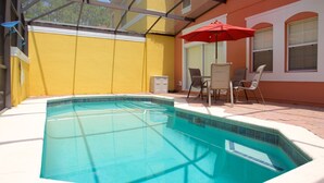 A swimming pool with a tiled edge, surrounded by a patio area with chairs and a red umbrella. - Durham Townhome with Pool at Encantada (Kissimmee)