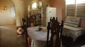 A dining area with a table set for four, a kitchen in the background, and a sign indicating the hotel name and location. - Hostal Rio De Agua Vivo (Trinidad)