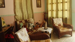 A cozy living room with a sofa, two wicker chairs, a small table, and various stuffed animals. - Hostal Rio De Agua Vivo (Trinidad)