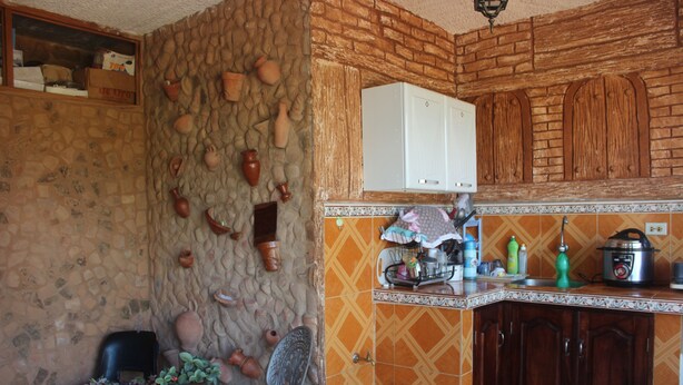 A kitchen with stone walls, wooden cabinets, and a dining area with a table and chairs. - Hostal Rio De Agua Vivo (Trinidad)