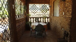 A patio with a table and chairs, a wooden bench, and a stone wall. - Hostal Rio De Agua Vivo (Trinidad)