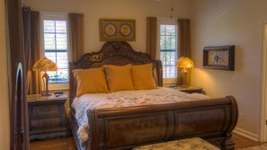 A bedroom with a wooden bed, two bedside lamps, a nightstand, a window with curtains, and a wall clock. - The Wakefield Vacation Home with Pool (Kissimmee)