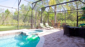 A covered outdoor swimming pool with lounge chairs and a table, surrounded by a glass enclosure. - The Wakefield Vacation Home with Pool (Kissimmee)