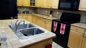 Una cocina con armarios de madera, un lavamanos de acero inoxidable, una estufa negra y un microondas.