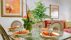 A dining table set with orange napkins, clear glassware, and a centerpiece of green plants.