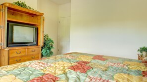 Un dormitorio con un armario de madera que contiene un televisor, una cama con colcha colorida y una planta en maceta.