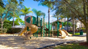 A playground with slides and climbing structures, surrounded by trees and a sandy ground. - Clovelly Condo at Windsor Palms Resort (Kissimmee)
