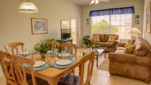 A dining area with a wooden table set for four, a sofa, and a television in the background. - Clovelly Condo at Windsor Palms Resort (Kissimmee)