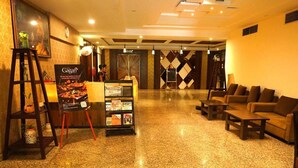 Eine Hotlellobby mit einer Rezeption, einer Sitzecke und einem Plakat, das das Restaurant Gagan bewirbt.